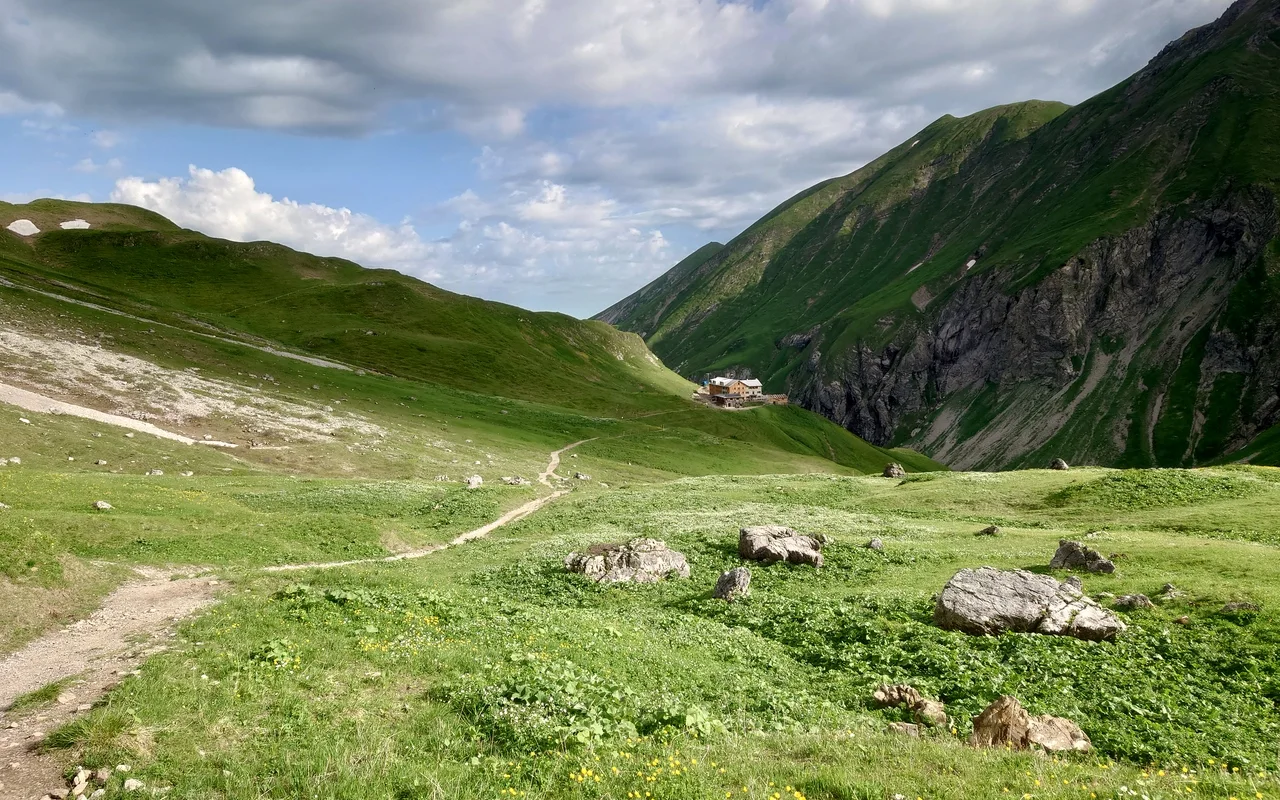 Wanderpfad über grüne Berghänge zur Kemptner Hütte unter steilen Felsflanken