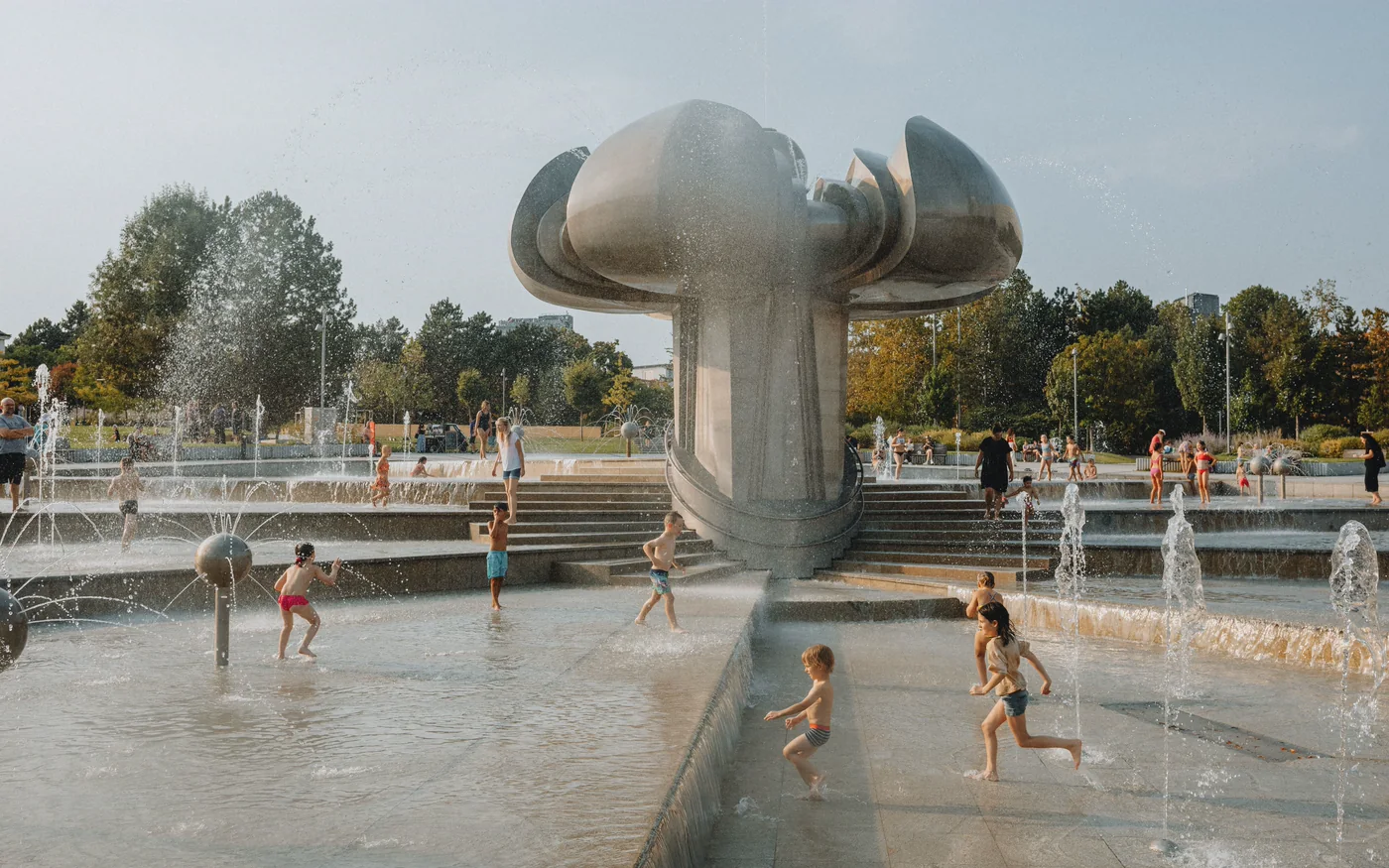 Kinder spielen zwischen Wasserfontänen einer städtischen Brunnenanlage