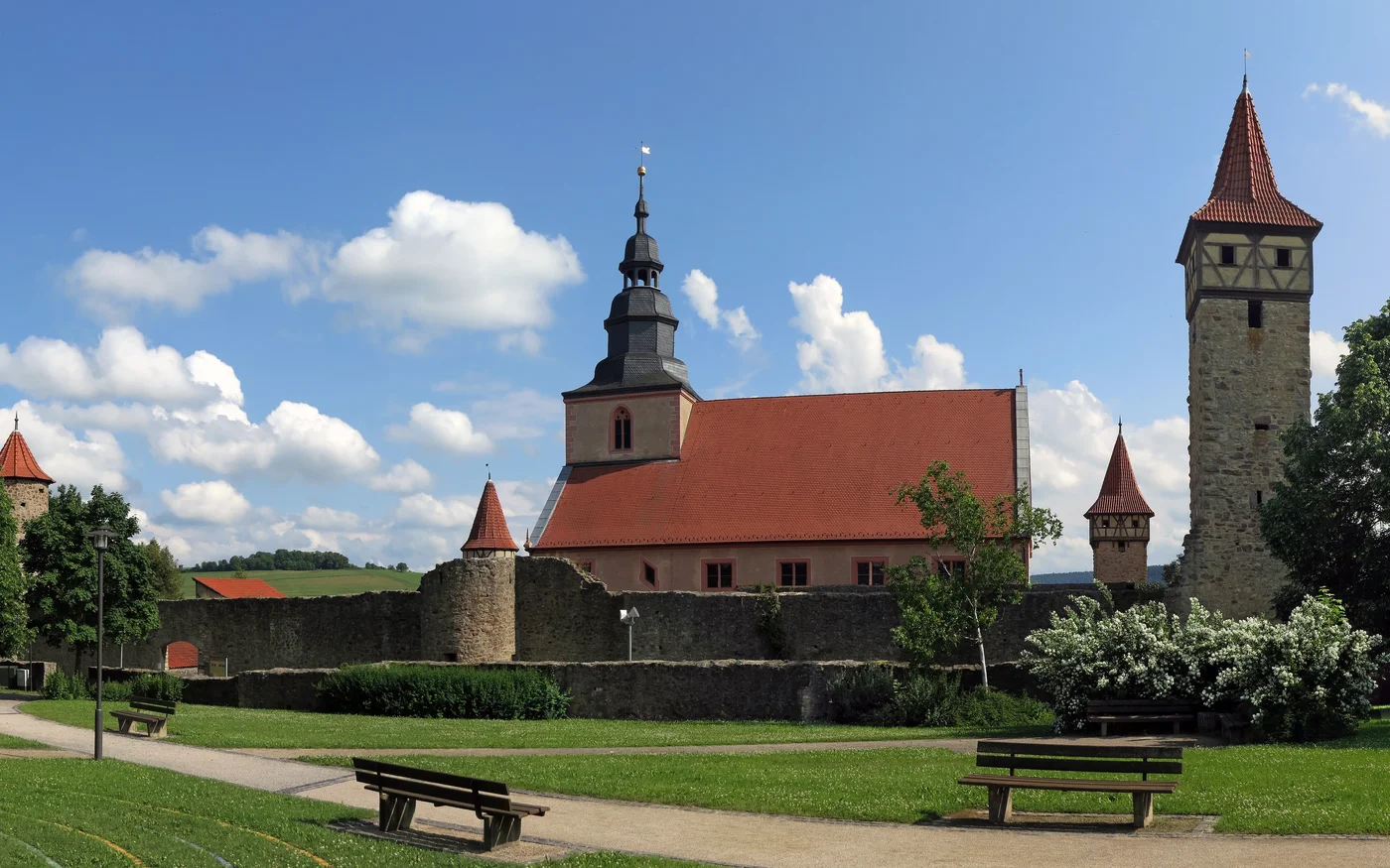 Kirche und Fachwerkgebäude hinter den steinernen Mauern der Kirchenburg Ostheim