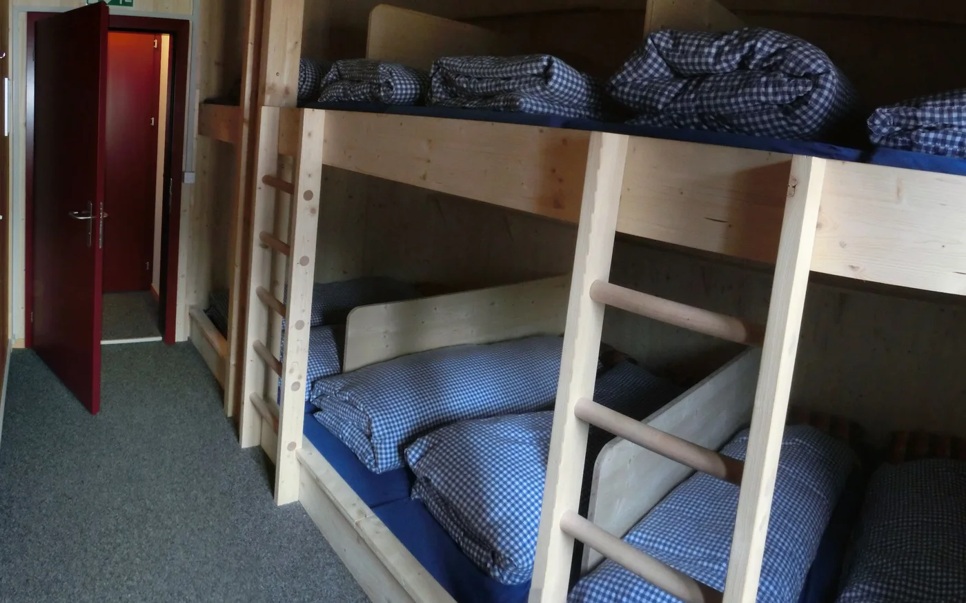 Hölzerne Etagenbetten mit Leitern, Kissen und kariertem Bettzeug im Schlafraum der Muttseehütte