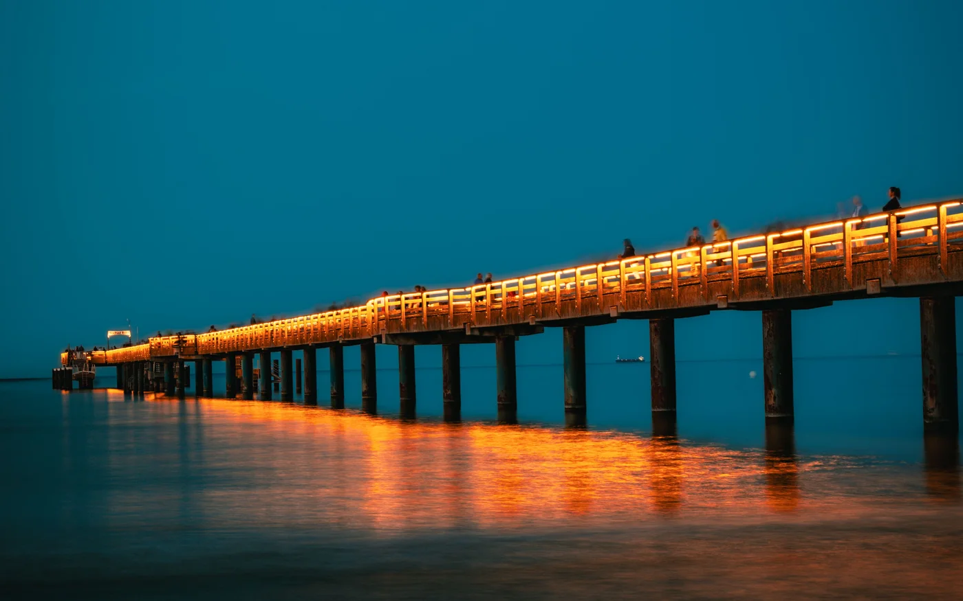 Orange beleuchtete Seebrücke von Binz über ruhigem Ostseewasser am blauen Abendhimmel