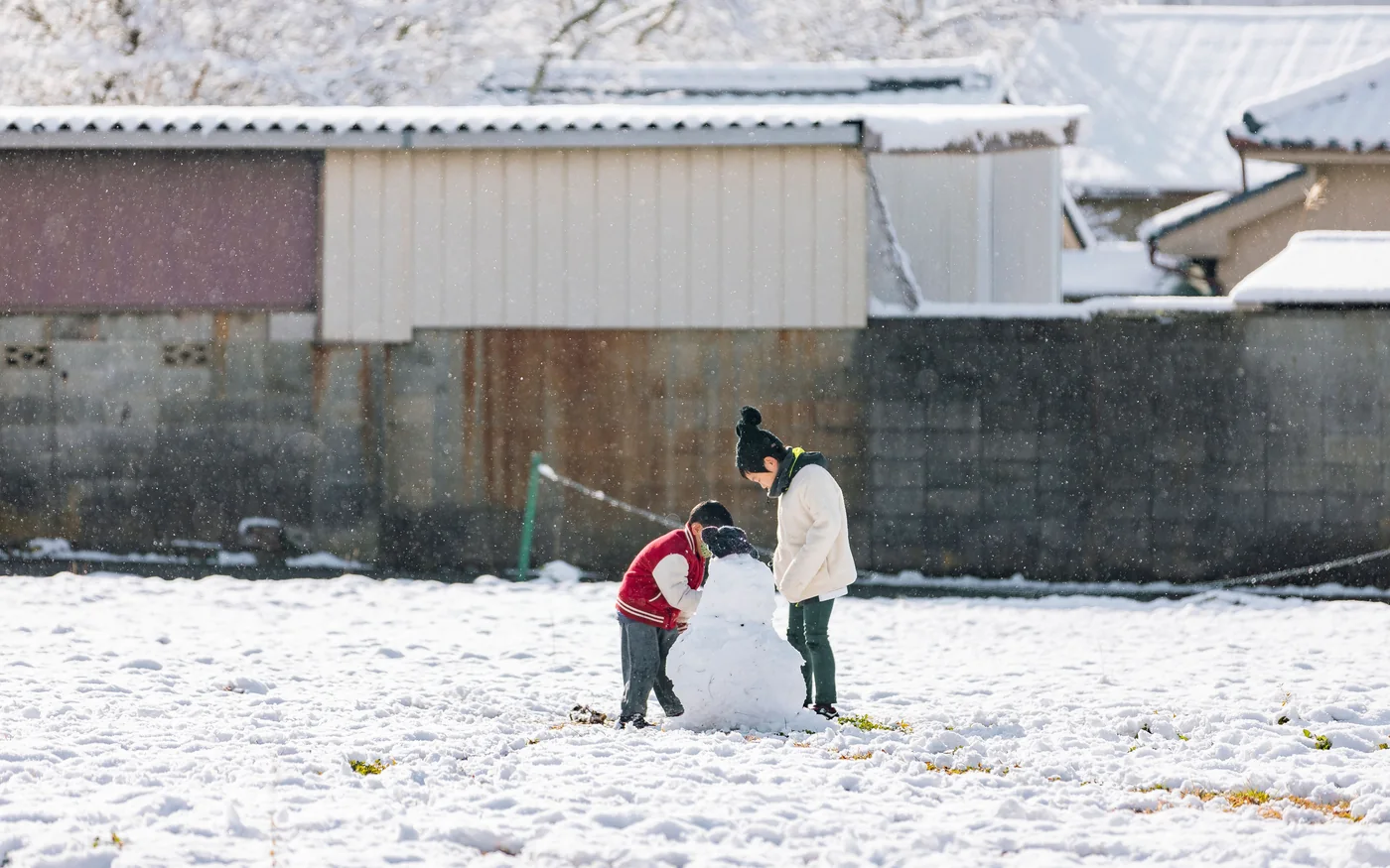 Zwei Kinder bauen im Schneefall gemeinsam einen Schneemann